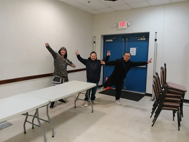 Three volunteers posing playfully beside folding tables and stacked chairs in a community room